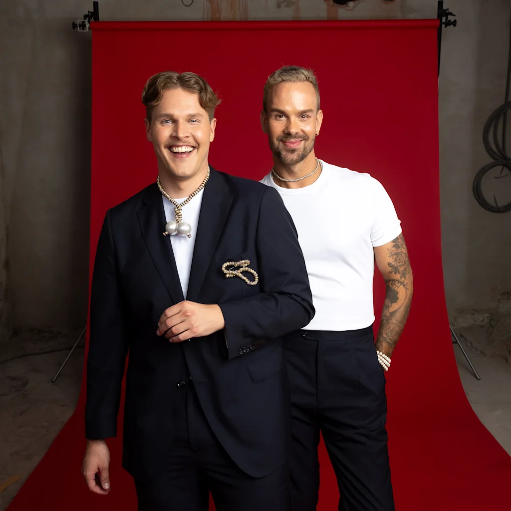 To smilende personer poserer for et bilde foran en levende rød bakgrunn, ser glade og engasjerte ut.