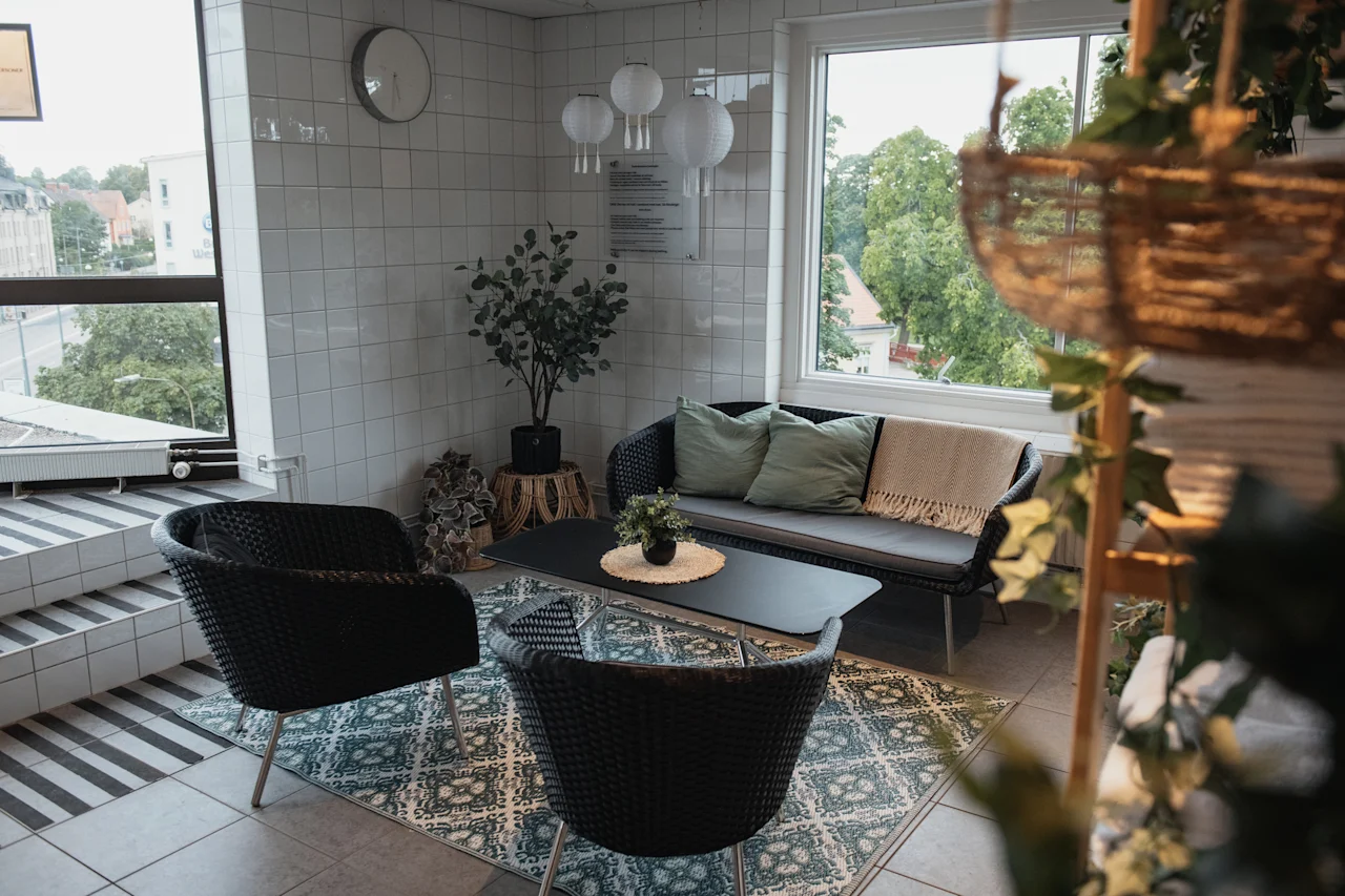 An inviting lounge space featuring comfortable seating, a coffee table, and lush greenery, with a bright window view.