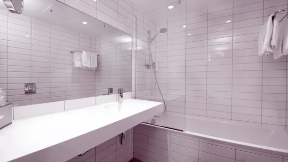 Et moderne, flislagt badeværelse med et vask, spejl og et badekar med bruser.