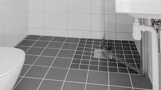 A modern bathroom with white tiles, glass shower enclosure, and black tiled floor.
