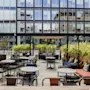 Outdoor seating area at Home Hotel Uppsala with tables, chairs, and lush green plants, set against a modern building. Text: 27.