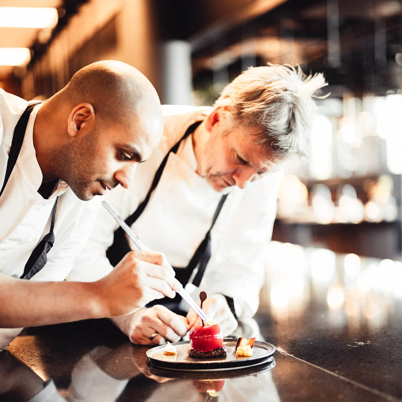 Två kockar dekorerar en dessert i ett restaurangkök.