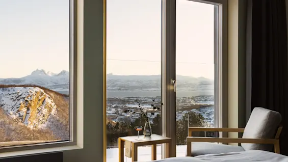 Et hyggeligt værelse med stort vindue og fantastisk udsigt over snedækkede bjerge, vand og en charmerende by.