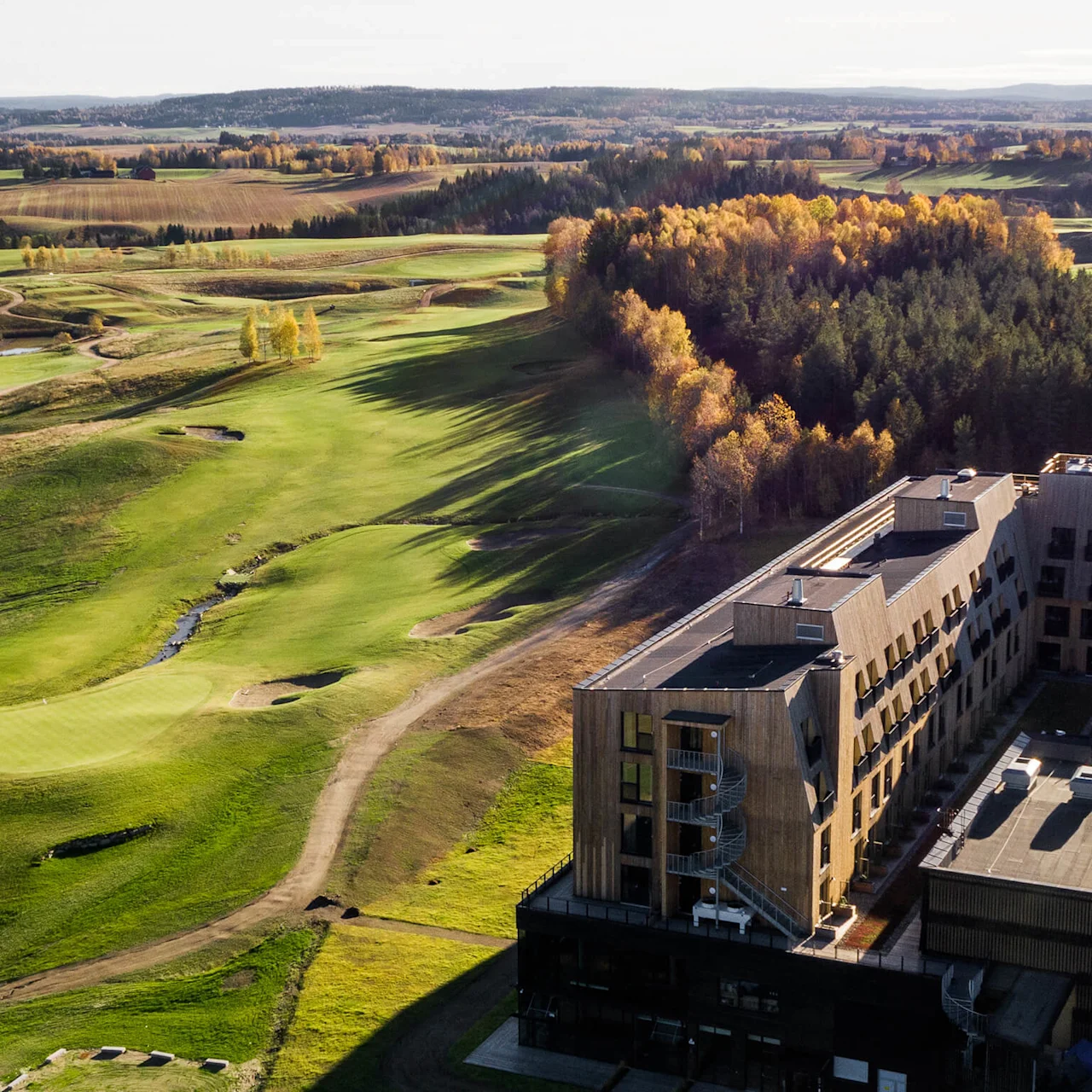 Flygbild av en golfbana intill en flervåningsbyggnad i ett höstlandskap.