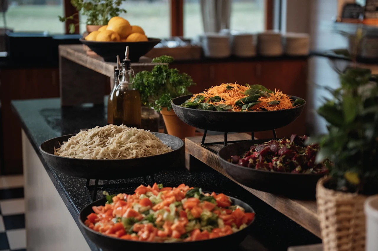 A vibrant buffet spread featuring fresh salads like shredded carrots with spinach, beet salad, and chopped tomatoes.