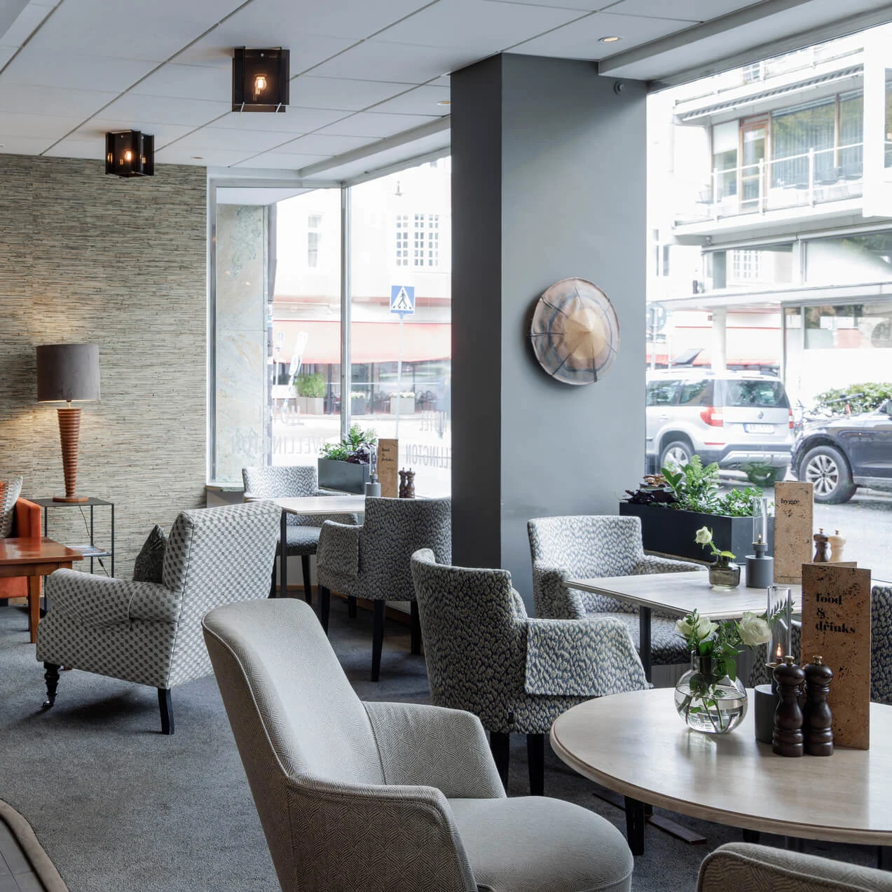 Mönstrade fåtöljer och bord inreder en hotelllobby med stora fönster som vetter mot en stadsgata.
