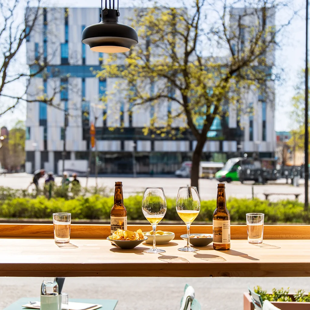 A table with drinks and snacks by a window, offering a view of a city street and a modern building.
