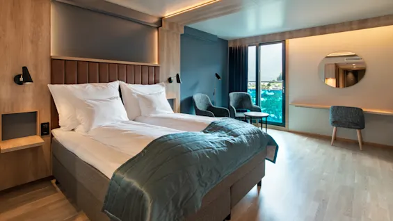 Et moderne hotelværelse med to senge, balkon med udsigt over vand og stilfuld indretning i træ og blåt.
