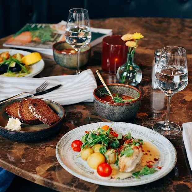Ett urval av rätter på ett bord dukat för en måltid med glas vatten, antyder en restaurangmiljö.