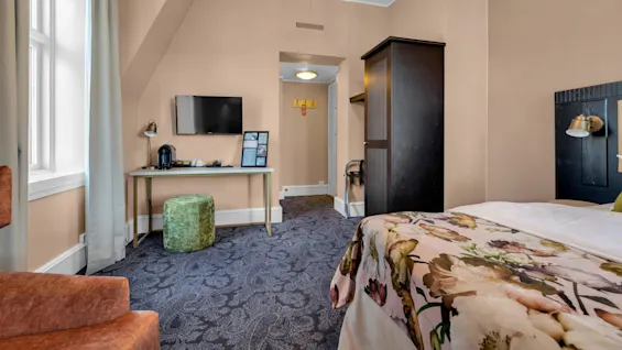 Ett välbelyst hotellrum med en säng, skrivbord, stol och tv.