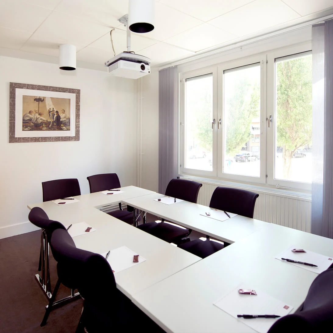 A conference room with a long table, chairs, and presentation equipment, bright illumination, framed artwork on the wall, and a sideboard with refreshments.