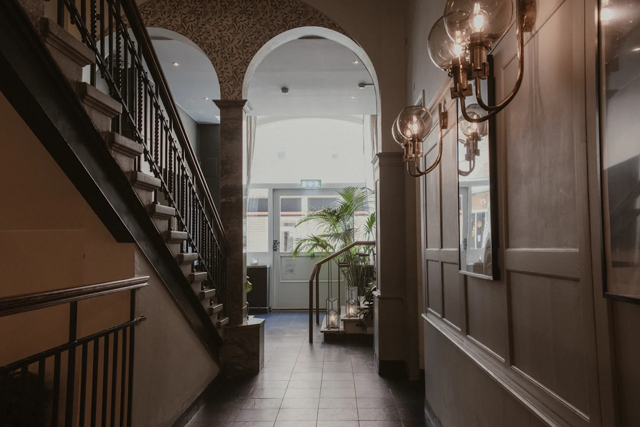 En klassisk hotellobby med en storslået trappe, buede gange og varm belysning, der skaber en indbydende atmosfære.