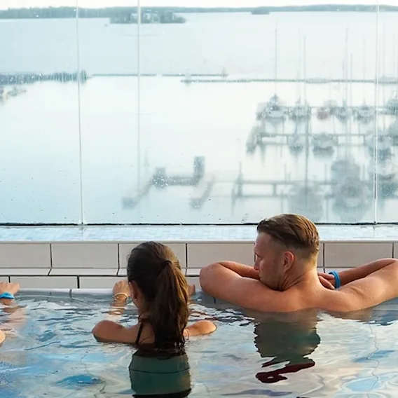 Människor kopplar av i en pool och njuter av en naturskön utsikt över en marina med båtar på vattnet.