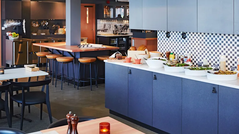 Modern kitchenette with a counter bar, stools, and a buffet spread in a clean, well-lit space.