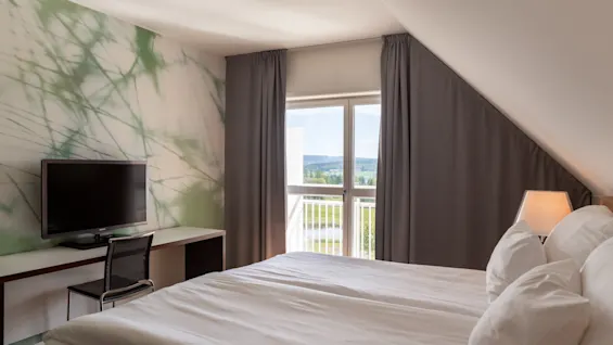 Et hyggeligt hotelværelse med en stor seng, et skrivebord med TV og et vindue med en naturskøn udsigt.