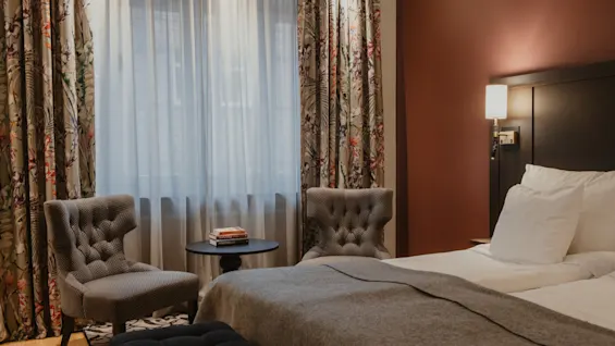 A cozy hotel room at Home Hotel Kung Oscar with a bed, two chairs, and a table with books, inviting relaxation.