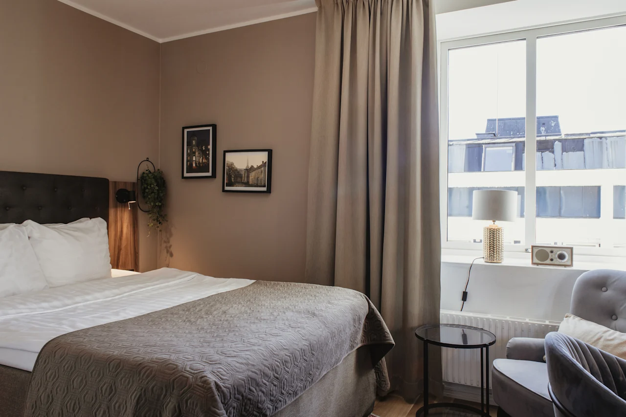 Ett mysigt hotellrum med en bekväm säng, ett stort fönster och en sittgrupp, perfekt för avkoppling.