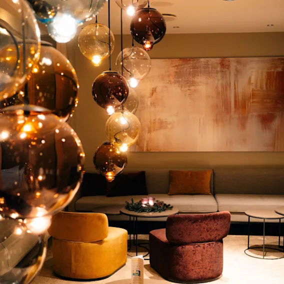 Et stilfullt sitteområde i en hotellobby med fargerike fløyelsstoler og lavthengende ravfargede glasslamper.