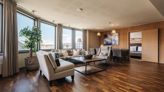 Rymlig hotellsvit med en bekväm soffgrupp, stora fönster och dörröppning in till sovrummet.