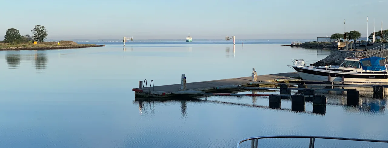 En rolig havnescene med stille vann, båter fortøyd ved en brygge og en fjern øy, som gjenspeiler den fredelige atmosfæren på Quality Hotel Öresund i Landskrona.