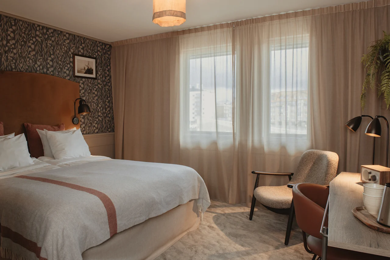 Et hyggeligt hotelværelse med en komfortabel seng, et skrivebord til arbejde eller afslapning og et lyst vindue, der slipper naturligt lys ind.