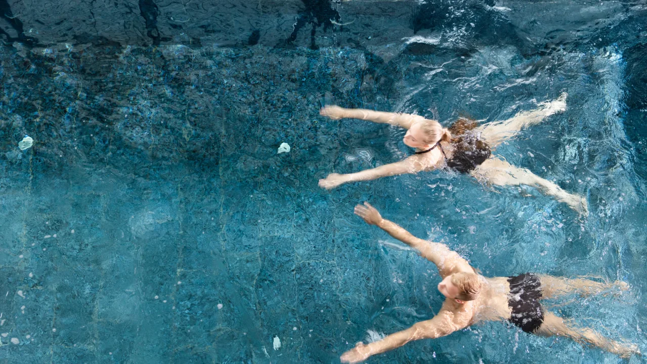 Two people swimming underwater in a clear blue pool.