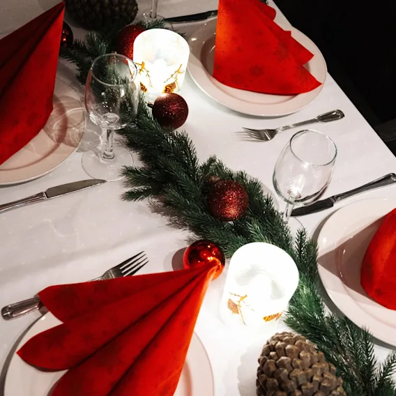 Et festlig dekket bord for høytidsmåltid, med røde servietter, vinglass, grønn girlander, pynt og lys.