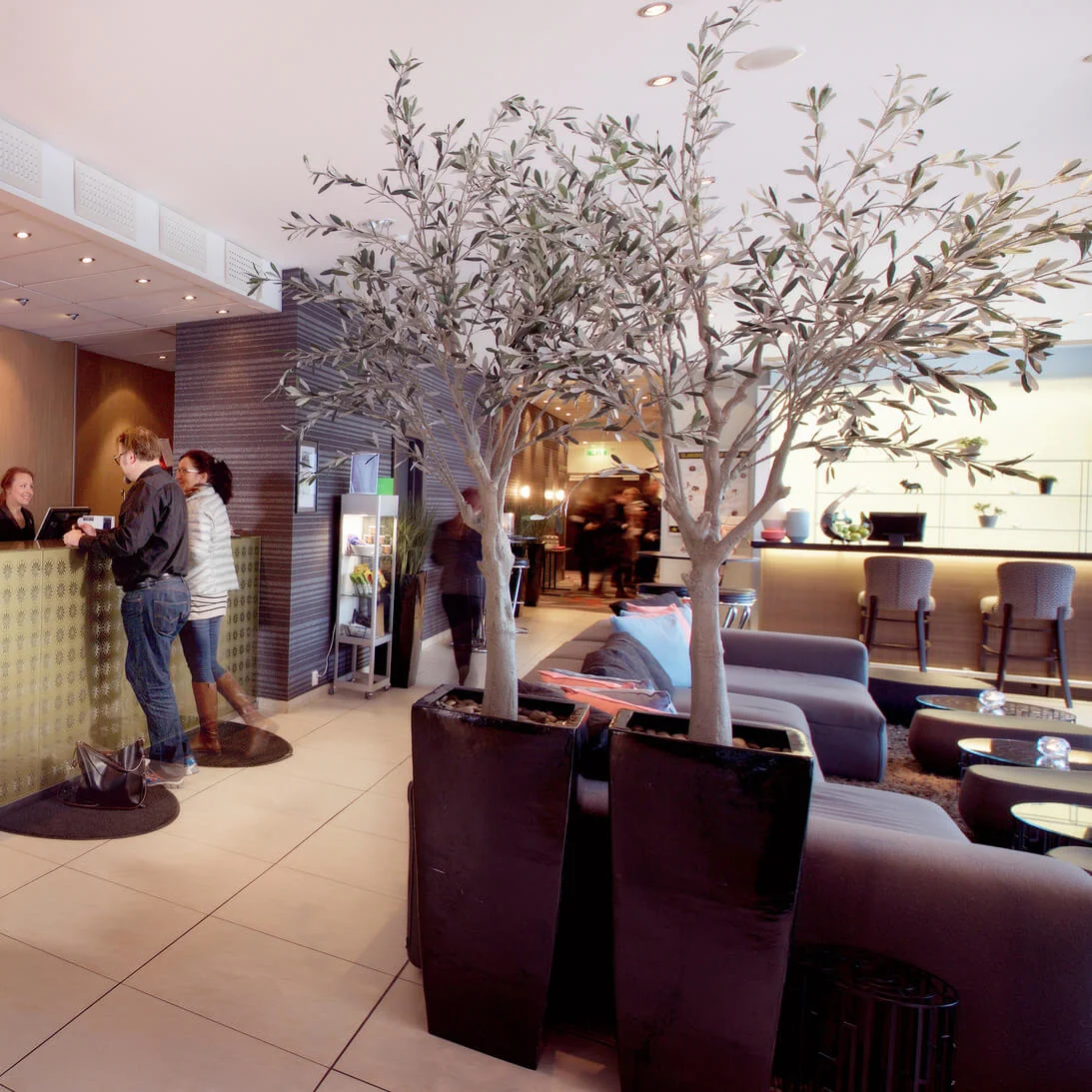 Two guests are checking in at a modern hotel reception desk, with staff assisting them.