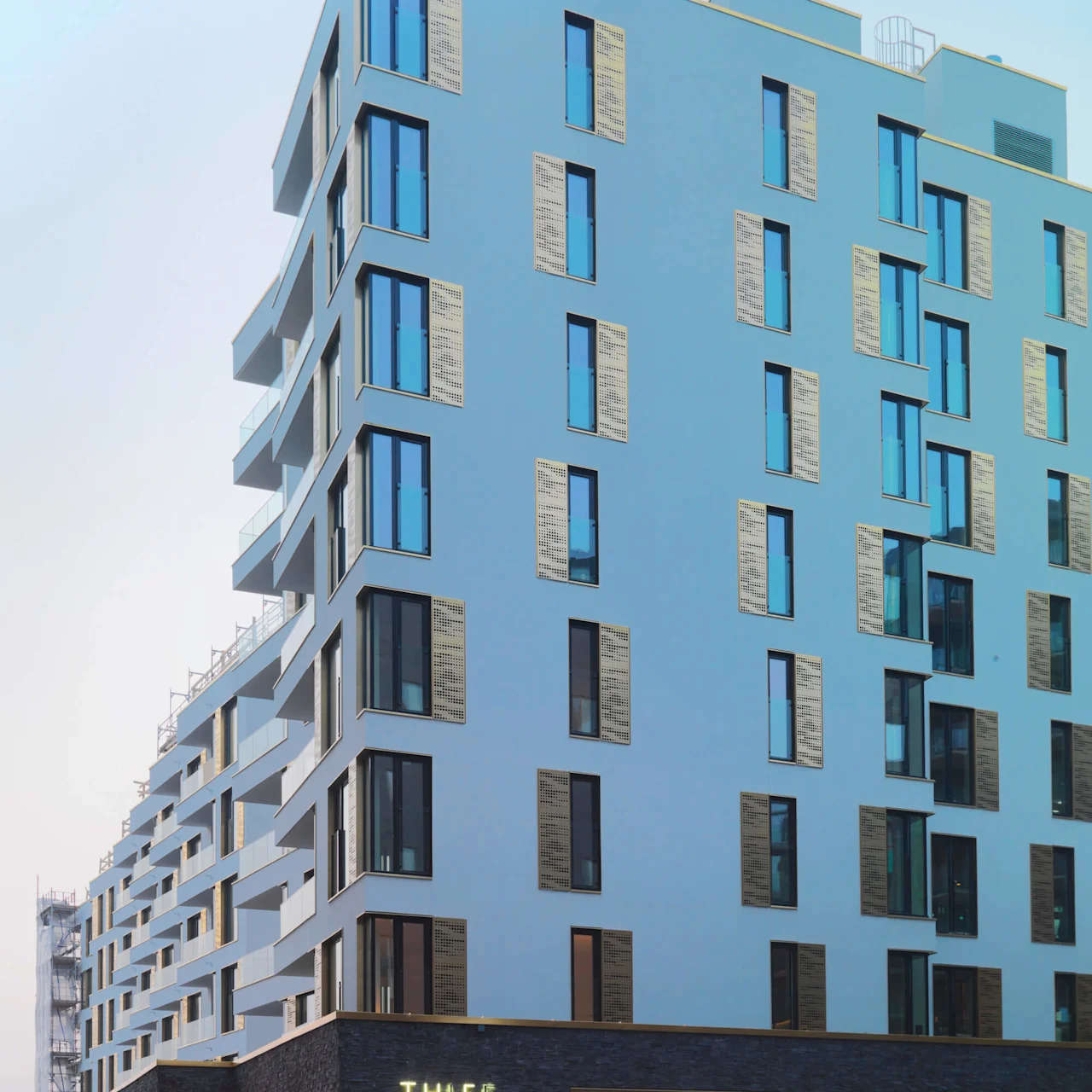 En moderne fleretasje bygning med store vinduer står under en klar himmel. Inngangen på bakkenivå har opplyst skilt med teksten "THIEF SPA," i en ryddig urban setting.