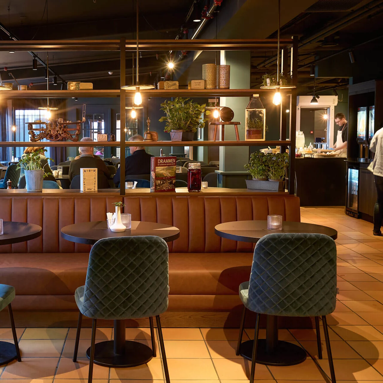 En hyggelig restaurantinteriør med lædersofaer, elegante stole og moderne belysning, flere siddende gæster.