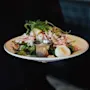 A plate of shrimp salad with lemon wedges, fresh greens, and a side of dressing is held by a person in a dimly lit restaurant.