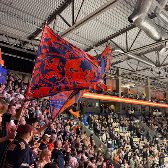Supporters som viftar med stora orangea och blå flaggor på en fullsatt inomhusarena under en match