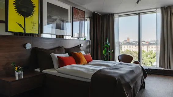 Clarion Hotel Sign - Stratum Suite. A stylish hotel room featuring a bed with colorful pillows and a panoramic city view.