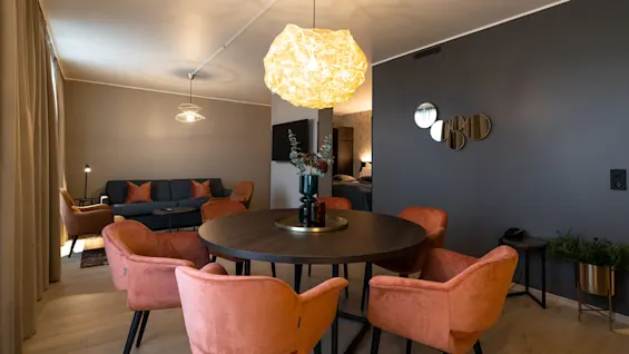Et rundt bord med dekorative genstande står i en moderne stue. Omkranset af orange stole og i nærheden en grå sofa. Blød belysning og moderne dekoration forbedrer den hyggelige atmosfære.