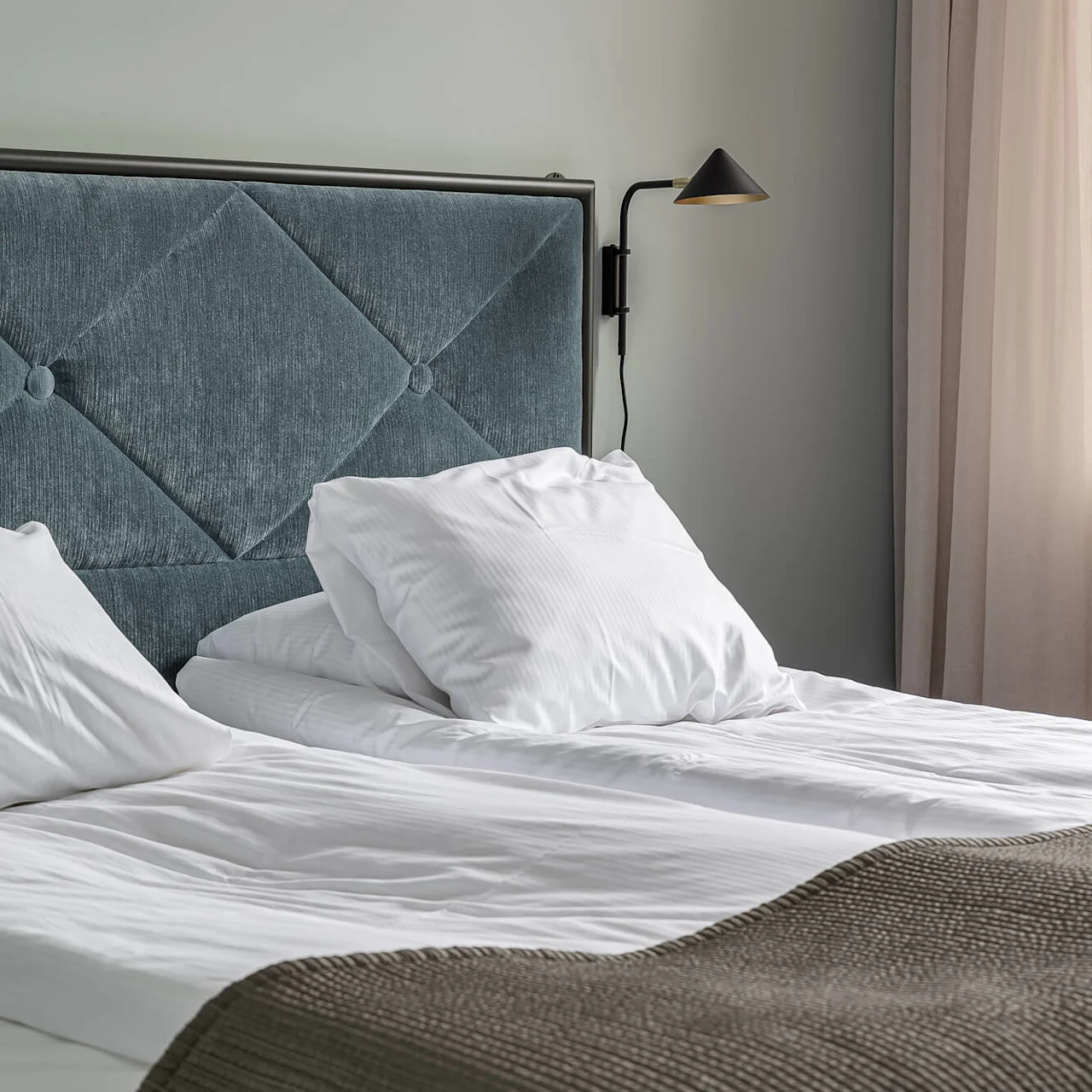 A neatly made bed with white linens; plush headboard, warm lighting, serene décor.