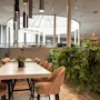 An inviting dining area at Home Hotel Grand Bodø featuring modern tables, comfortable seating, a lush green wall, and a bright skylight.