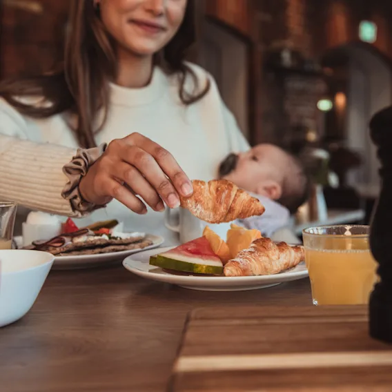 En person håller ett barn och äter frukost med croissanter, frukt och juice.