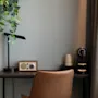 En koselig skrivebordsplass med en plante, en moderne lampe, en radio i vintagestil og en kaffemaskin, ved siden av en komfortabel stol.