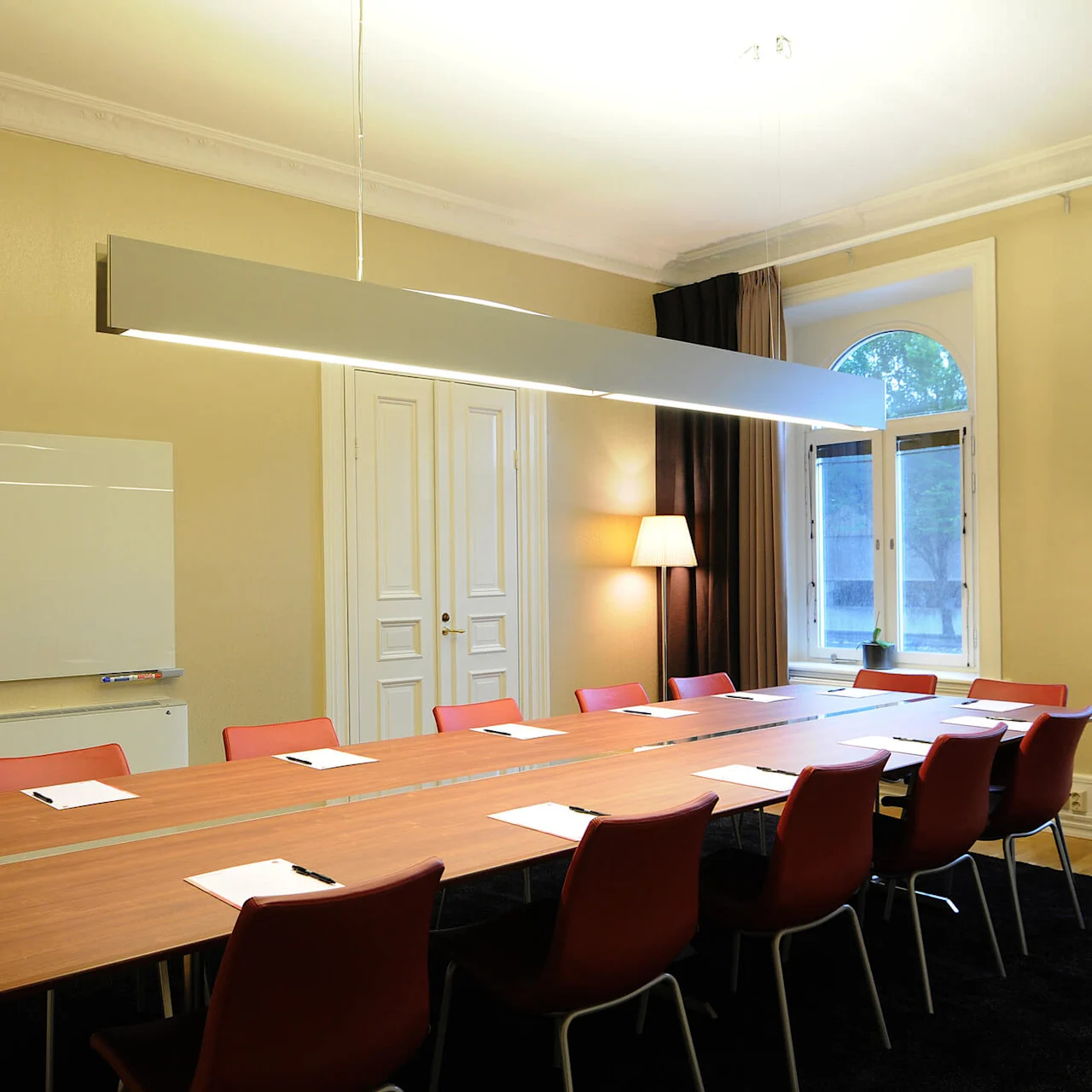A conference room with a long table and chairs, papers on the table, and a whiteboard on the wall.