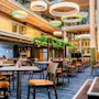 Ett rymligt hotellatrium med matbord, moderna cirkulära lampor och frodiga gröna växter, vilket skapar en inbjudande atmosfär.