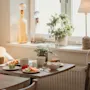 A cozy breakfast spread on a table by a sunlit window, with fresh fruit, a sandwich, and drinks.