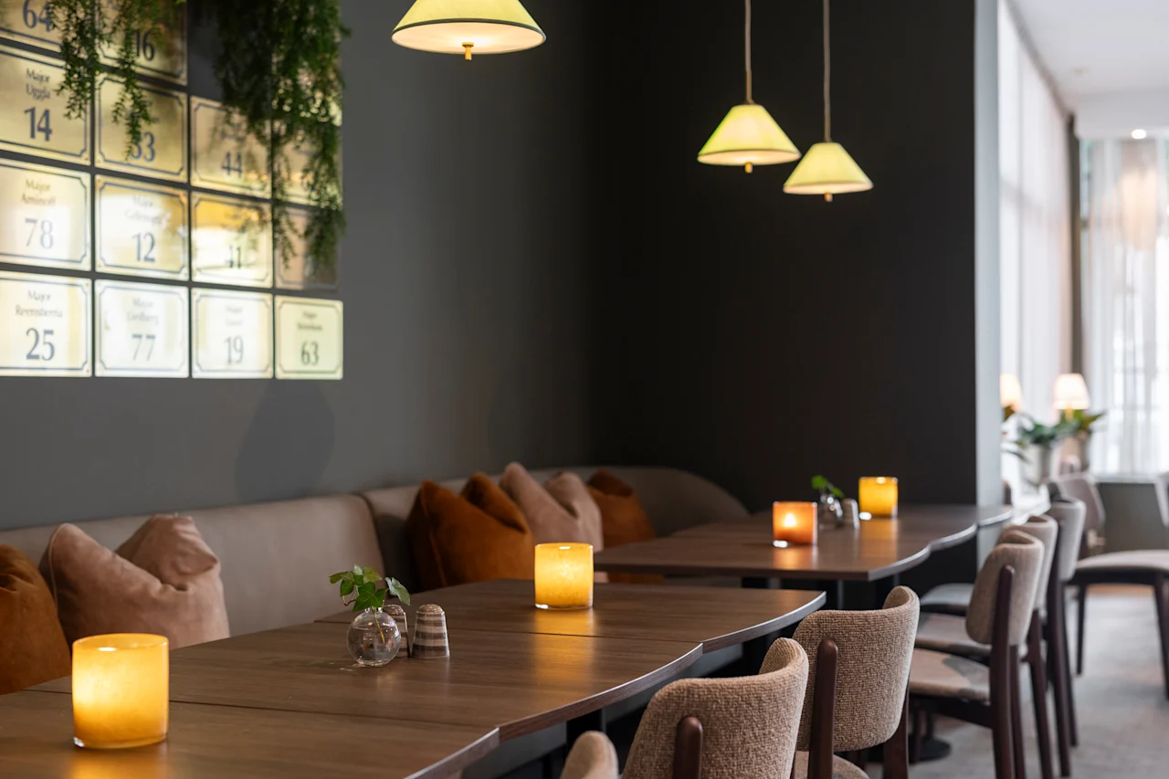 Viihtyisä ravintola, jossa on lämmin valaistus, puupöytiä ja penkkipaikkoja. Seinälaatoissa näkyy nimiä kuten Maja ja numeroita kuten 14, 78.