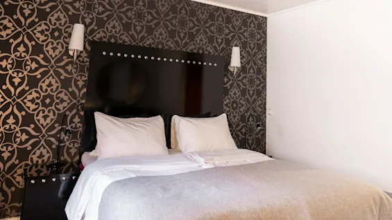 Viihtyisä makuuhuone, jossa on suuri sänky, kuviollinen tapetti ja pehmeä valaistus, täydellinen rentoutumiseen.