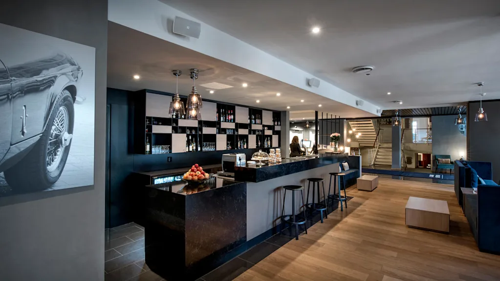 Modern bar with stools, pendant lights, and artwork in a stylish interior with wood floors and a staircase.