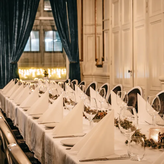 An elegantly set long dining table with white tablecloths and folded napkins in a classic banquet room.