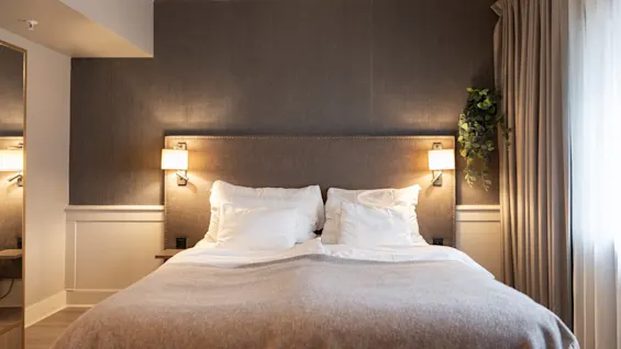 A cozy bedroom at Home Hotel Grand Bodø with a large bed, soft pillows, and warm lighting, perfect for relaxation.