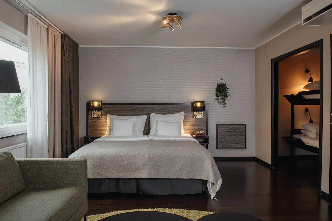 A cozy hotel room featuring a large bed, a comfortable sofa, and a separate bunk bed area for additional guests.