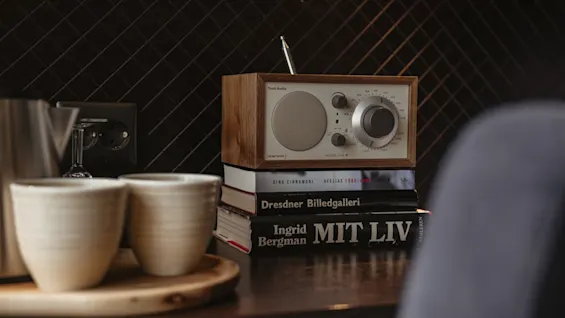 En mysig hotellrumsmiljö med en vintage radio ovanpå böcker inklusive Gina Cinnamoni och Ingrid Bergman Mit Liv, tillsammans med två koppar.