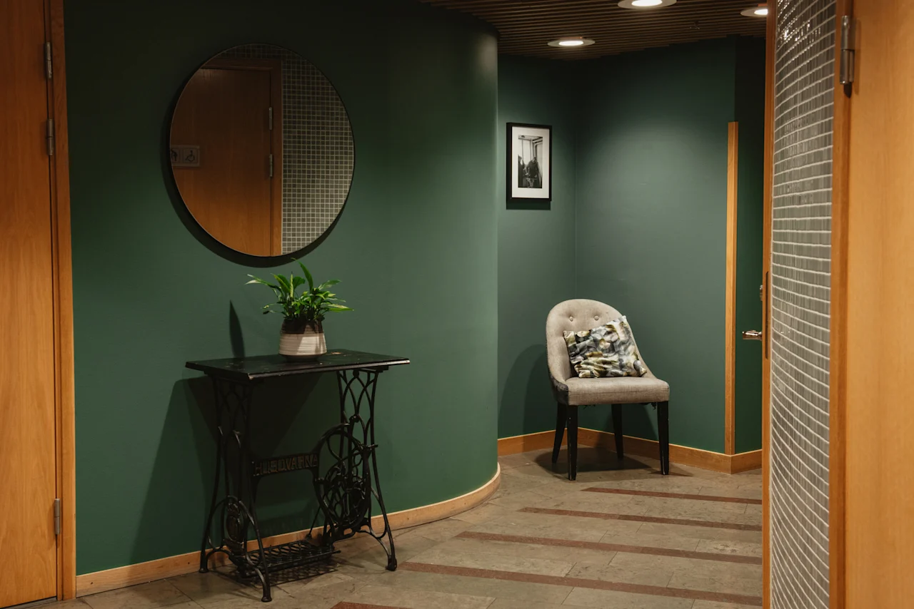 A cozy corner in the Home Hotel Uppsala with dark green walls, a vintage table, a potted plant, and a comfortable chair.