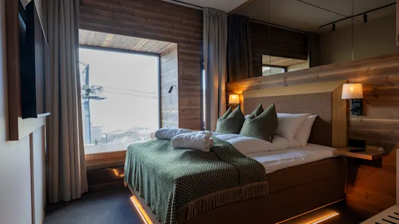 Ett mysigt hotellrum med stort fönster mot en snöig skidort. Har en bekväm säng och varm träinredning.